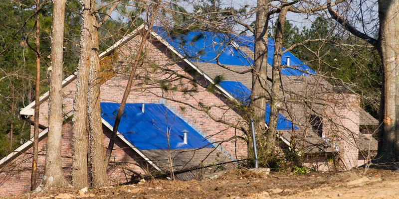 tornado damaged house with a blue tarpaulin on the roof